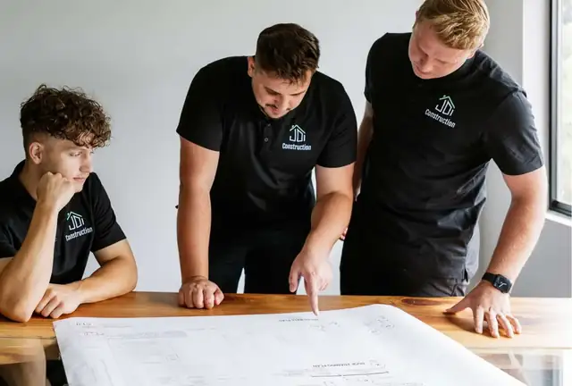 Three JDI Construction team members in company shirts reviewing remodel plans at a table